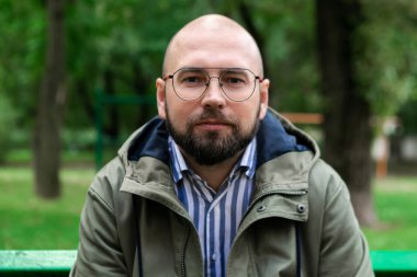 Sakallı ve gözlüklü genç adam parkta poz veriyor, moda adamı, açık hava portresi, yakın çekim.