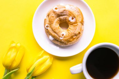 Bir buket lale, tatlı çörek ve sarı arka planda kahve fincanı.