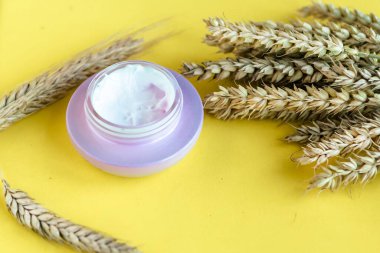 Parlak sarı arka planda kozmetik kavanozu ve buğday kulakları 