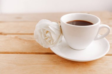 Kahve fincanı ve ahşap arka planda beyaz gül.