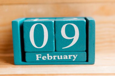 9 Şubat. Ahşap zemin üzerinde ay ve tarih olan mavi küp takvimi.