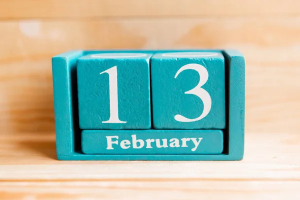 February 13. Blue cube calendar with month and date on wooden background.