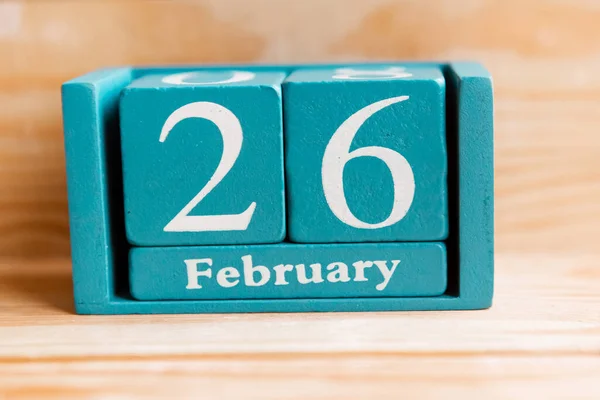 February 26. Blue cube calendar with month and date on wooden background.