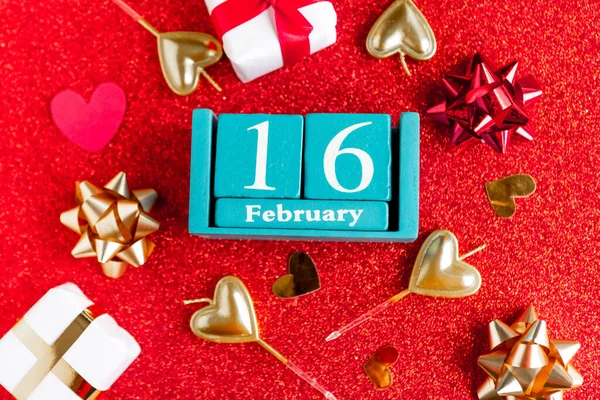 stock image February 16. Blue cube calendar with month and date and decorations on red glitter background. 