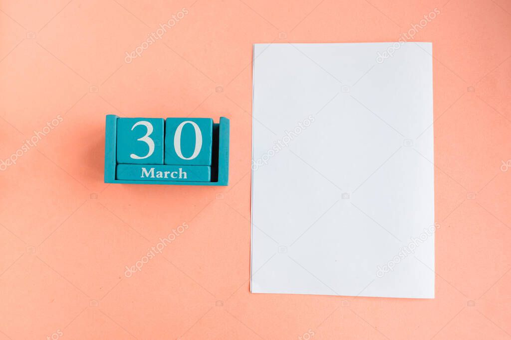 March 30. Blue cube calendar with month and date and white mockup blank on pink background. 