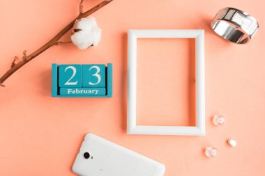23 Şubat. Pembe pastel arka planda ay, tarih ve resim çerçeveli mavi küp takvimi.