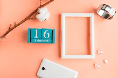16 Şubat. Pembe pastel arka planda ay, tarih ve resim çerçeveli mavi küp takvimi.