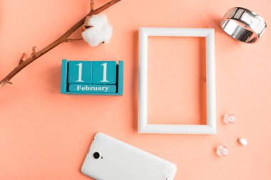 11 Şubat. Pembe pastel arka planda ay, tarih ve resim çerçeveli mavi küp takvimi.