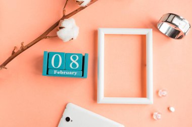 8 Şubat. Pembe pastel arka planda ay, tarih ve resim çerçeveli mavi küp takvimi.