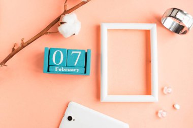 7 Şubat. Pembe pastel arka planda ay, tarih ve resim çerçeveli mavi küp takvimi.