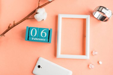 6 Şubat. Pembe pastel arka planda ay, tarih ve resim çerçeveli mavi küp takvimi.