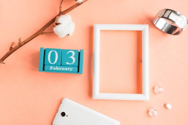 3 Şubat. Pembe pastel arka planda ay, tarih ve resim çerçeveli mavi küp takvimi.