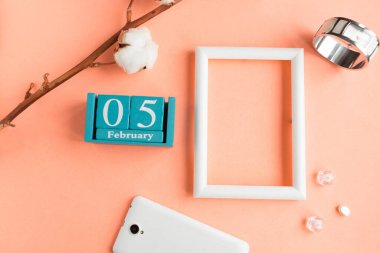 5 Şubat. Pembe pastel arka planda ay, tarih ve resim çerçeveli mavi küp takvimi.