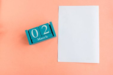 2 Mart. Aylık ve tarihli mavi küp takvimi ve pembe arkaplanda beyaz model boş.