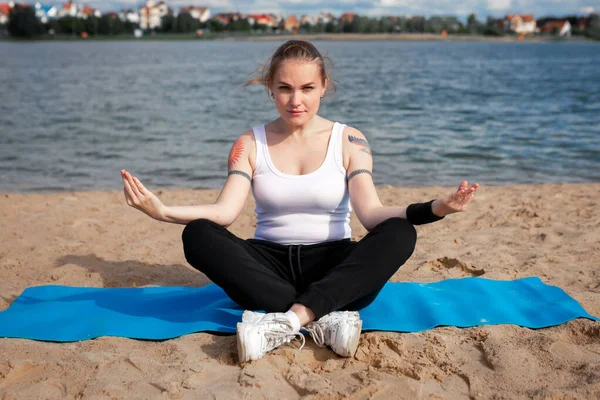 Exercise equipment, Woman wearing face mask is rolling yoga mat on the sea beach, outdoor sport during the coronavirus concept