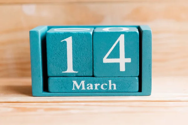 March 14. Blue cube calendar with month and date on wooden background.