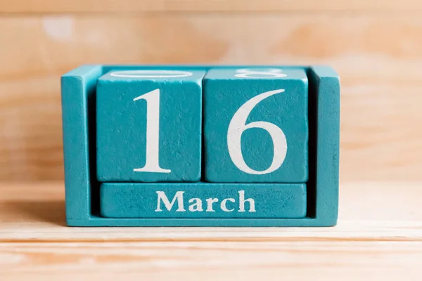 March 16. Blue cube calendar with month and date on wooden background.