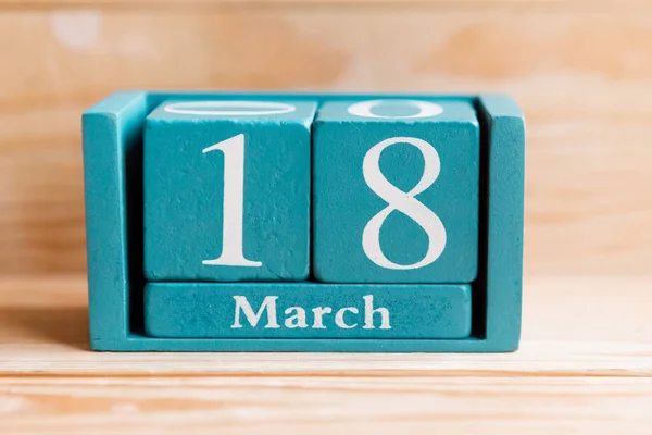 March 18. Blue cube calendar with month and date on wooden background.