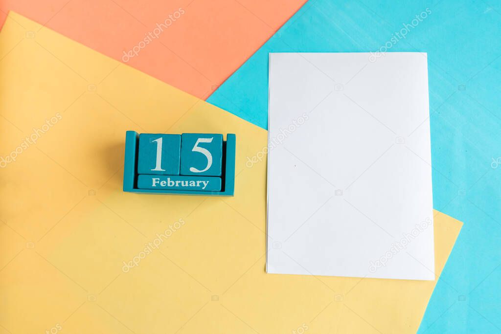 February 15. Blue cube calendar with month and date and white mockup blank on color geometric background.
