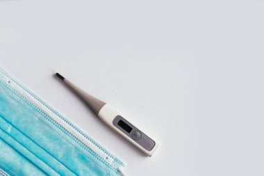 Beyaz arkaplanda termometre ve yüz tıbbi maskesi, metin için kopyalama alanı