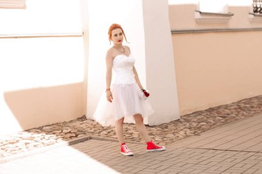 Genç ve güzel bir gelinin portresi. Kırmızı spor ayakkabılı. Elinde gül buketi var.