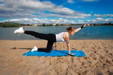  Egzersiz ekipmanları, yüz maskesi takan kadın deniz sahilinde yoga minderi sallıyor. Coronavirus konsepti sırasında açık hava sporu.