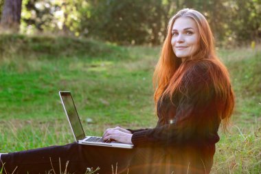 Doğada serbest çalışan biri. Kadın ormanda dizüstü bilgisayarla çalışıyor..