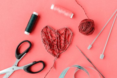 Sevgililer Günü El Yapımı Kırmızı İplik Kalbi ve pembe arka planda dikiş malzemeleri. Aşk Tatili. Düğün konsepti. 