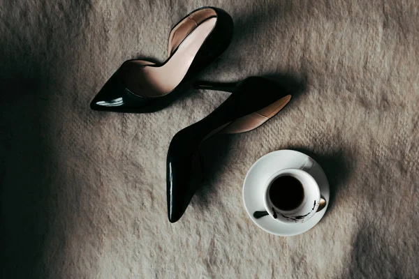 Flat lay photo with classic high-heeled shoes and half-finished coffee on the bed