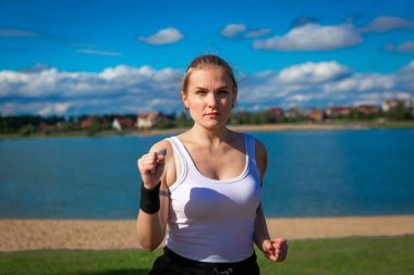 Yüz koruyucu maskeli genç kadın nehir kıyısında egzersiz yapıyor. Koronavirüs salgını sırasında açık havada spor faaliyetleri. Spor doğada