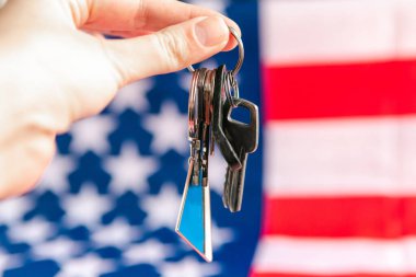 Bir kadının eli, Amerikan bayrağında beyaz bir oyuncak evi tutuyor. ABD konseptinde kiralık konutlar