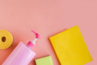 Pembe bulaşık deterjanı ve pembe arka planda süngerlerle dolu bir şişe. Minimum konsept. Boşluğu kopyala