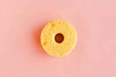 Pembe arka planda bulaşık yıkamak için yuvarlak sarı sünger. Asgari konsept