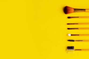 Parlak sarı arka planda farklı kozmetik makyaj fırçaları. Metin için alanı kopyala