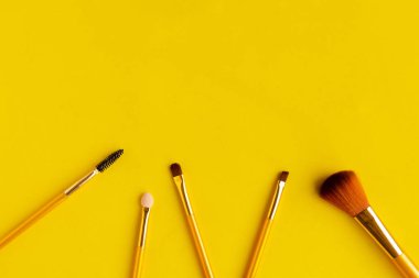 Parlak sarı arka planda farklı kozmetik makyaj fırçaları. Metin için alanı kopyala