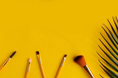 Parlak sarı arka planda farklı kozmetik makyaj fırçaları. Metin için alanı kopyala