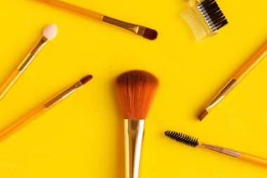Parlak sarı arkaplanda farklı kozmetik makyaj fırçaları.