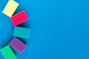 Mavi arka planda bulaşık yıkamak için çok renkli süngerler. Minimum konsept. Metin için alanı kopyala