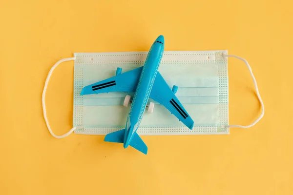 Toy airplane and face medical mask on yellow background. Travel during the coronavirus pandemic concept