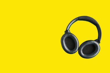 Parlak sarı arka planda izole edilmiş büyük siyah kulaklıklar. Metin için alanı kopyala