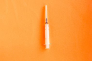 Parlak turuncu arka planda tıbbi şırınga. Üst görünüm, asgari