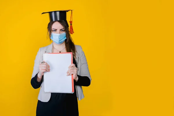 2021年卒業 若いですブルネットの女性の肖像画で顔医療マスクと大学の帽子でスタジオで黄色隔離された背景 — ストック写真