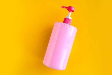 Bottle with pink dishwashing liquid on bright yellow background. Minimal concept