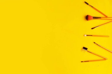 Parlak sarı arka planda farklı kozmetik makyaj fırçaları. Metin için alanı kopyala