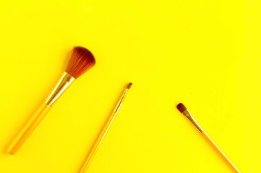 Parlak sarı arka planda farklı kozmetik makyaj fırçaları. Metin için alanı kopyala