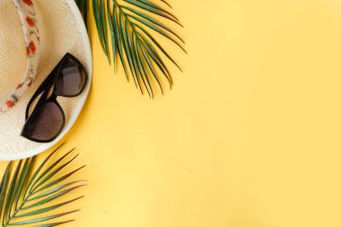 Straw hat, palm tree branches and sunglasses on bright yellow background. Summer vacation concept. Copy space, minimal