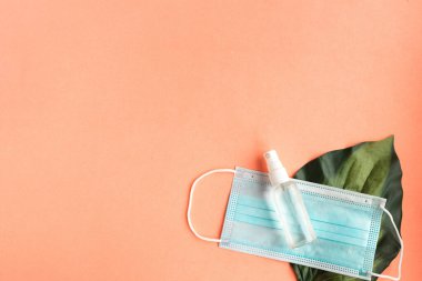 Face medical mask, hand sanitizer and tropical green leafs on pink pastel background minimal. Coronavirus travel. Summer vacations during the pandemic concept. Copy space