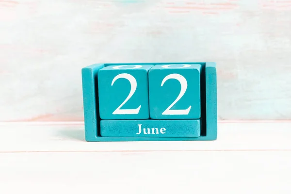 June 22. Blue cube calendar with month date isolated on wooden background.