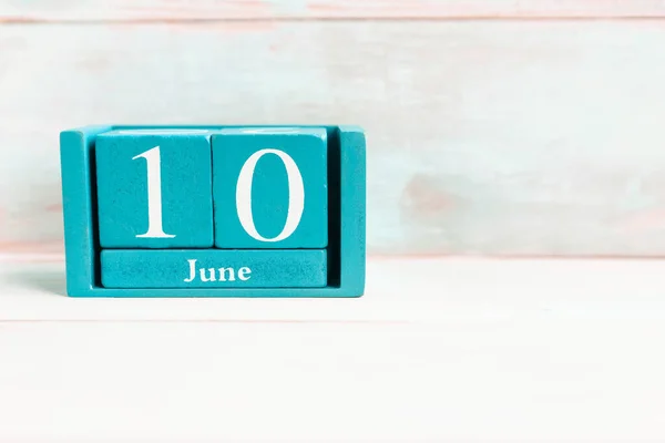 June 10. Blue cube calendar with month date isolated on wooden background.