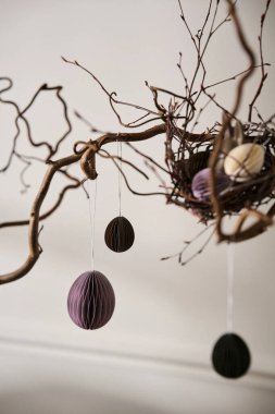 Paskalya 2026 bahar festivali iç kompozisyonu olarak düzenlenmiş ağaç dalı üzerindeki dekoratif kağıt süslemeleri doğal dokular ve minimalist mevsimsel stil ile